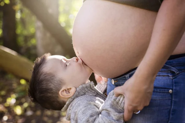 Glückliches Kind hält Bauch einer schwangeren Frau im Wald — Stockfoto