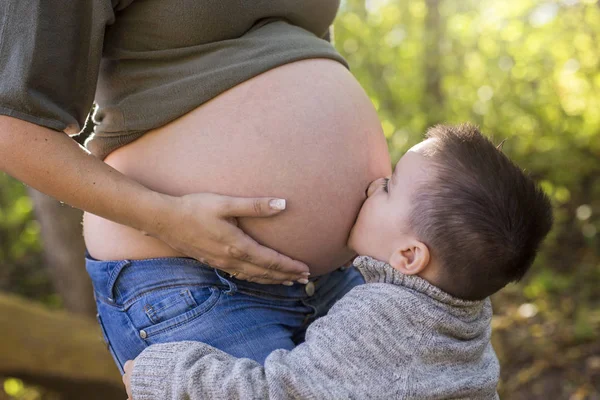 Šťastné dítě drží břicho těhotné ženy v lese — Stock fotografie