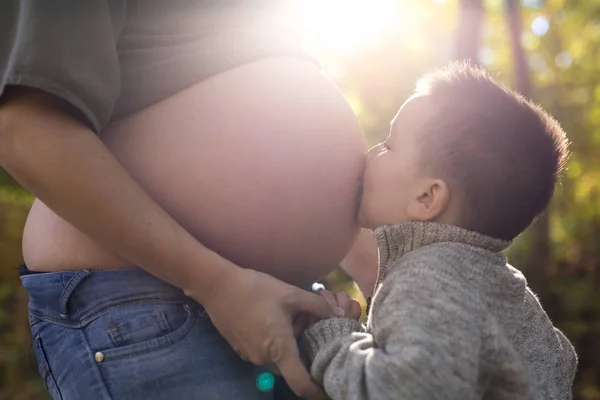 Šťastné dítě drží břicho těhotné ženy v lese — Stock fotografie