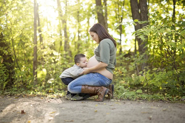Niño feliz sosteniendo el vientre de la mujer embarazada en el bosque — Foto de Stock