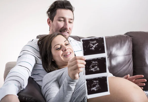 Budoucí rodiče při pohledu na ultrazvukové vyšetření na pohovce — Stock fotografie