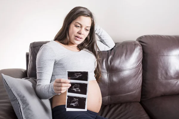 Schwangere betrachtet Ultraschallbild ihrer Babys im Wohnzimmer — Stockfoto