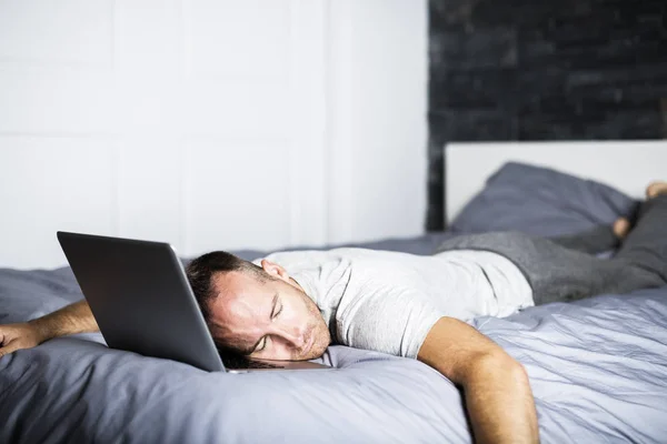 Hombre durmiendo sobre el ordenador portátil en la cama —  Fotos de Stock