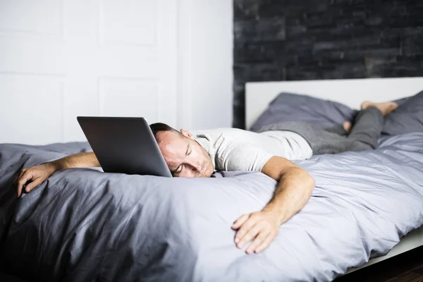 Человек спит за компьютером ноутбука в постели — стоковое фото