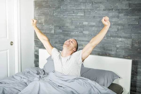 Веселый молодой человек просыпается в постели и вытягивает руки — стоковое фото