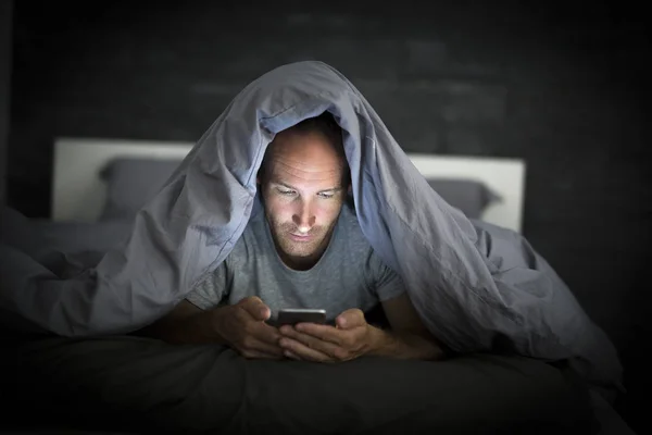 Joven adicto al teléfono celular hombre despierto tarde en la noche en la cama con teléfono inteligente —  Fotos de Stock