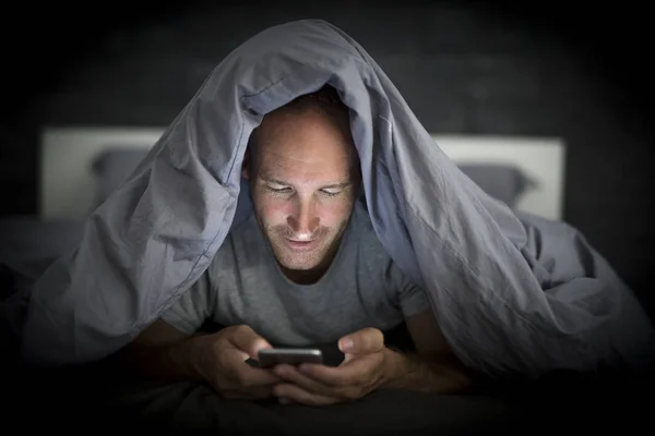 Mobil mladý narkoman muž vzhůru pozdě v noci v posteli pomocí smartphonu — Stock fotografie
