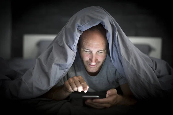 Jovem viciado em celular homem acordado tarde da noite na cama usando smartphone — Fotografia de Stock