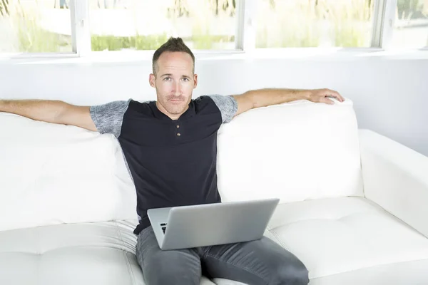 Вид спереди красивого человека, сидящего дома на диване с ноутбуком — стоковое фото