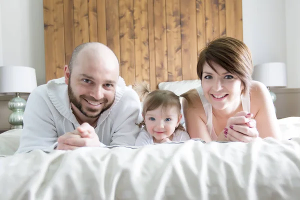 子供連れのご家族。幸せな親のベッドに赤ちゃんと遊ぶ — ストック写真