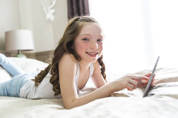 女の子のタブレット技術を自宅のベッドを横たわっていた。 — ストック写真