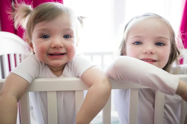 Menina bonito no berço no quarto do bebê com a irmã — Fotografia de Stock