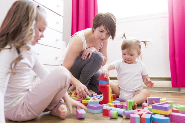 Menina criança em conjunto com a mãe e a irmã jogando brinquedos educativos — Fotografia de Stock