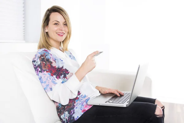 Prachtige blonde vrouw rusten op een witte Bank thuis en met behulp van een laptop — Stockfoto