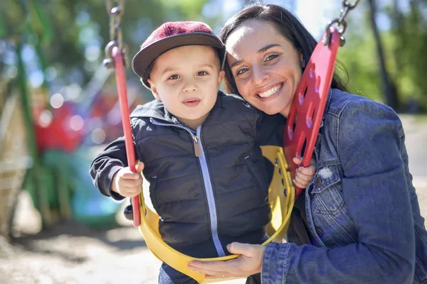 Glad mor driver son på swing i en park — Stockfoto