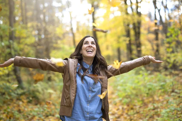 Счастливая женщина бросает осенние листья в парке — стоковое фото