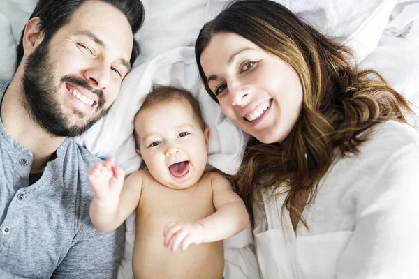 Mother father and baby child on a white bed. — Stock Photo, Image