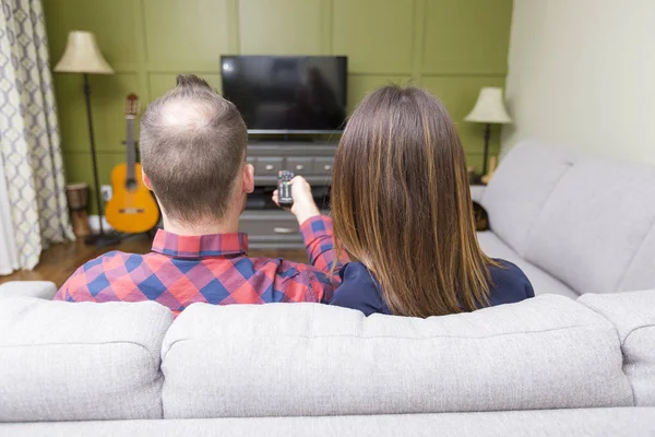 Beautiful couple watching TV sitting on couch at home — Stock Photo, Image