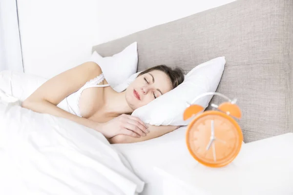 Young sleeping woman and alarm clock in bedroom at home — Stock Photo, Image