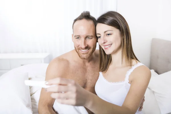 Веселая пара узнаёт результаты теста на беременность сидя на кровати — стоковое фото