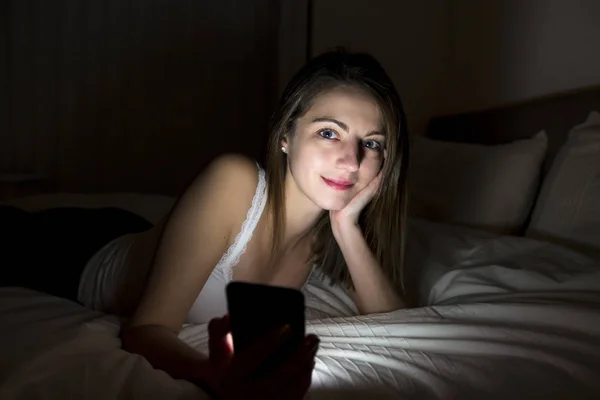 Woman using smartphone on bed at night — Stock Photo, Image