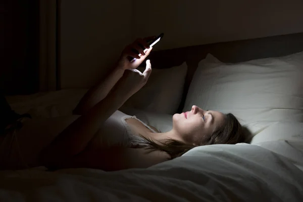 Woman using smartphone on bed at night — Stock Photo, Image