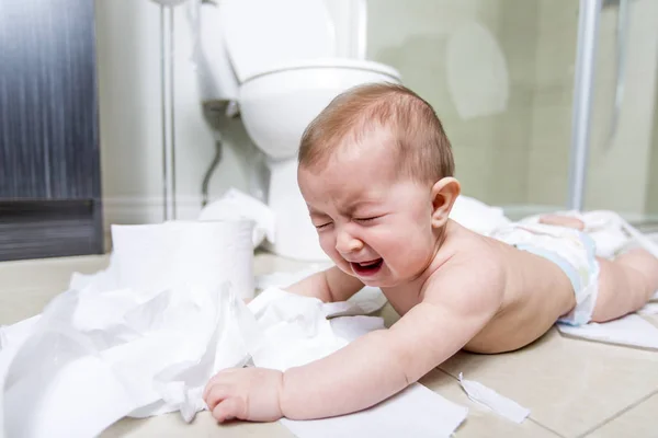 Toddler ripping up toilet paper in bathroom Stock Image