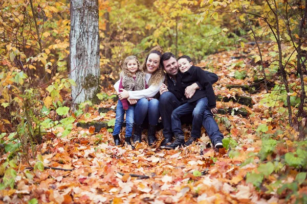 Familia de cuatro personas disfrutando de hojas doradas en el parque de otoño — Foto de Stock