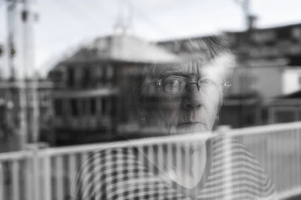 Donna anziana che guarda fuori da una finestra come una depressa — Foto Stock