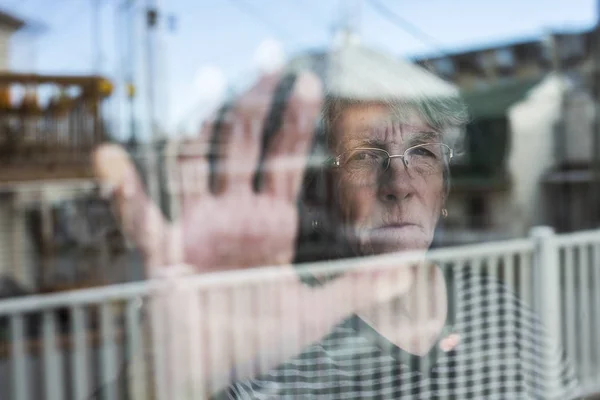 Senior vrouw op zoek door middel van een venster zoals drukken — Stockfoto