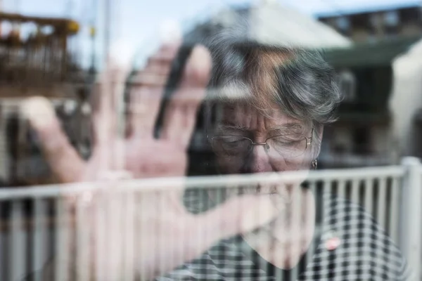 Donna anziana che guarda fuori da una finestra come una depressa — Foto Stock