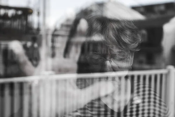 Donna anziana che guarda fuori da una finestra come una depressa — Foto Stock