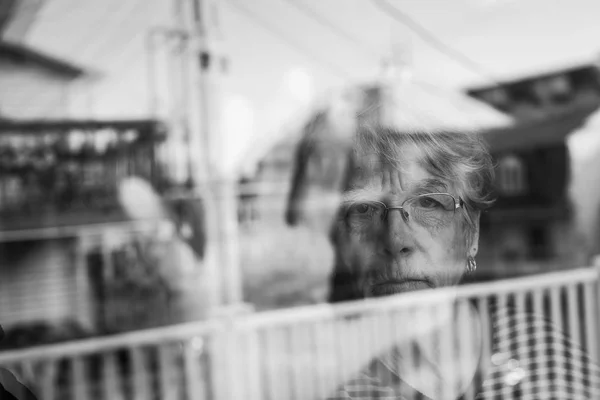 Donna anziana che guarda fuori da una finestra come una depressa — Foto Stock