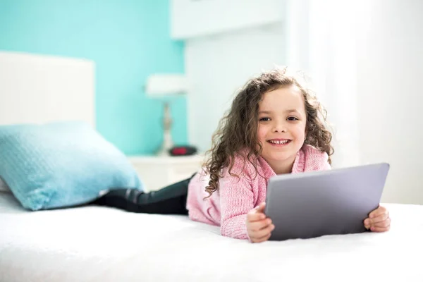 Technologie stają się łatwiejsze. cute dziewczynka trzymając cyfrowe tabletki i uśmiechając się leżąc w łóżku. — Zdjęcie stockowe