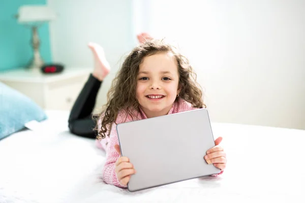 技術は容易になります。デジタル タブレットを保持し、ながらベッドで横になっている笑顔かわいい女の子. — ストック写真