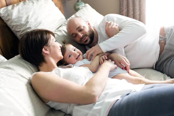Beautiful mother and handsome father with baby daughter lying on bedroom — Stock Photo, Image