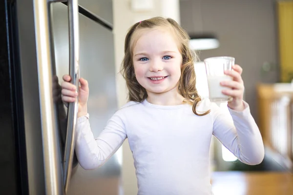 Jonge witte meisje verse melk drinken van een glas terwijl staan voor open koelkast. — Stockfoto