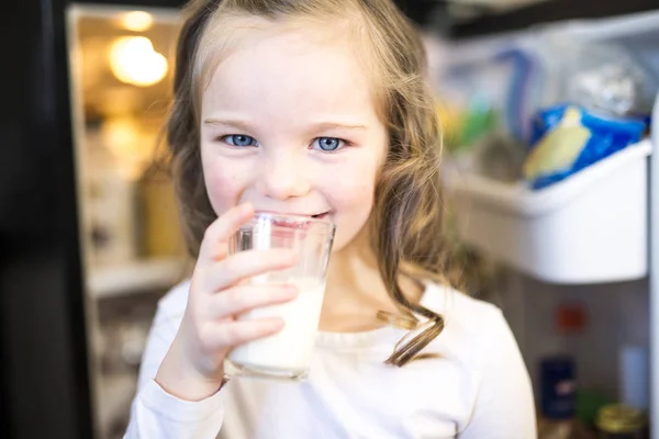 Jonge witte meisje verse melk drinken van een glas terwijl staan voor open koelkast. — Stockfoto