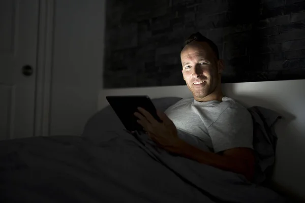 Człowiek pracuje w nocy, leżąc na łóżku — Zdjęcie stockowe