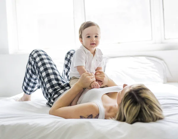 Hermosa joven madre e hijo acostados juntos en una cama — Foto de Stock