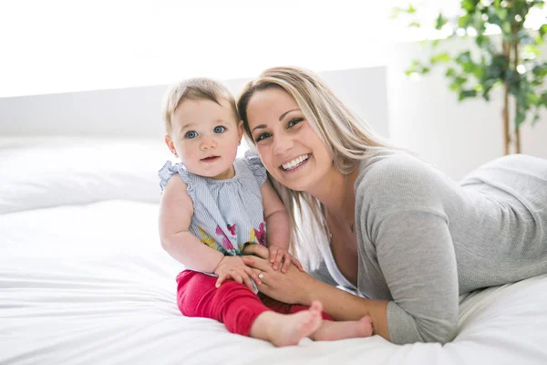 Bebê bonito sentar na mãe na cama de seda — Fotografia de Stock