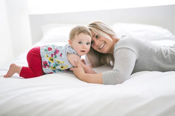 Bebê bonito sentar na mãe na cama de seda — Fotografia de Stock