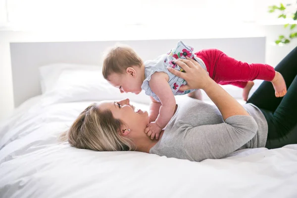 Bonito bebé sentarse en mamá en la cama de seda — Foto de Stock