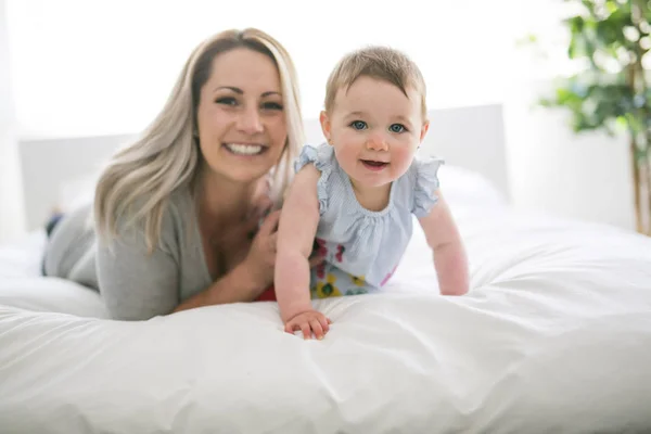 Bebê bonito sentar na mãe na cama de seda — Fotografia de Stock