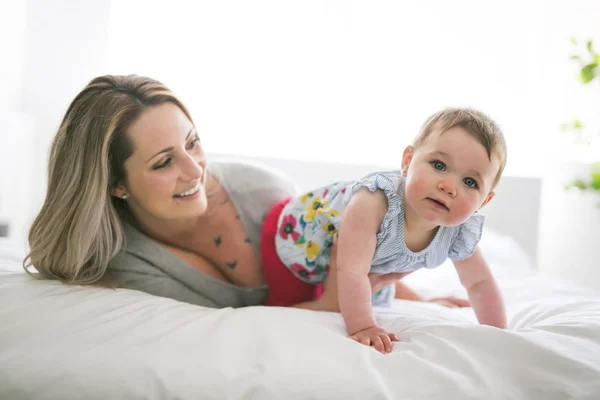 Bebê bonito sentar na mãe na cama de seda — Fotografia de Stock