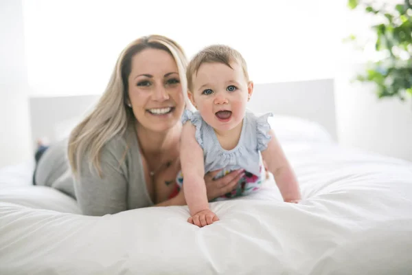 Bebê bonito sentar na mãe na cama de seda — Fotografia de Stock