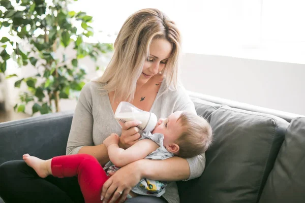 Feliz madre joven con la niña en el sofá en casa — Foto de Stock