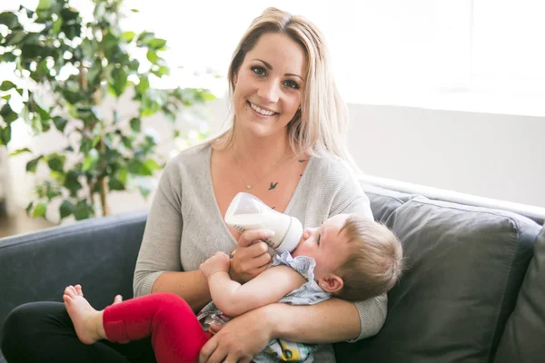 Glad ung mor med baby tjej på soffan hemma — Stockfoto