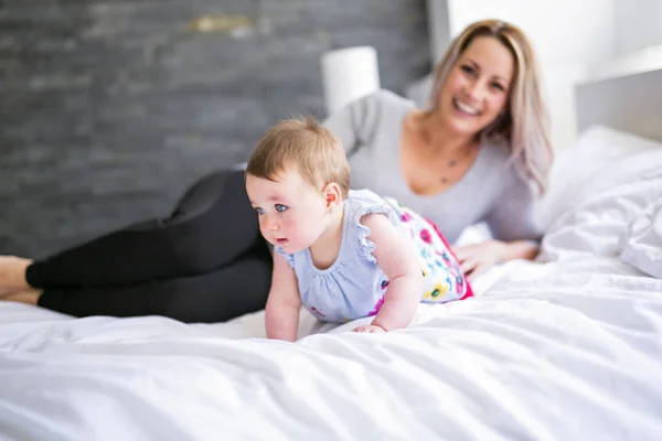 Bebê bonito sentar na mãe na cama de seda — Fotografia de Stock