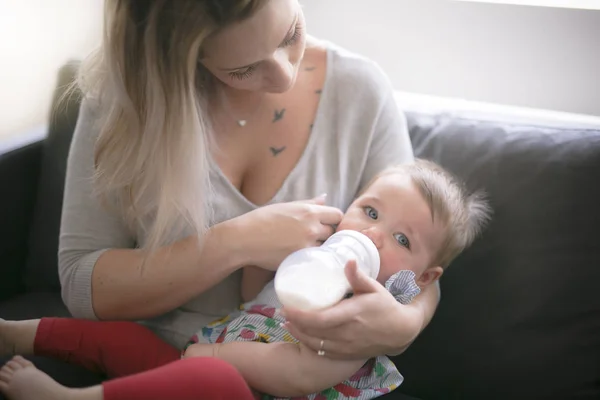 Feliz madre joven con la niña en el sofá en casa — Foto de Stock